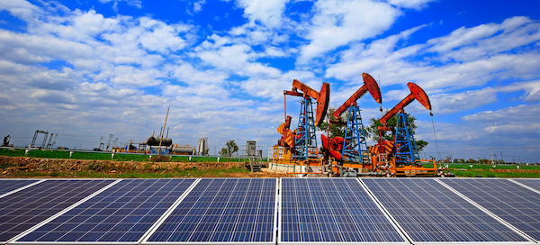 solar panels with oil rigs in background and a blue sky with clouds